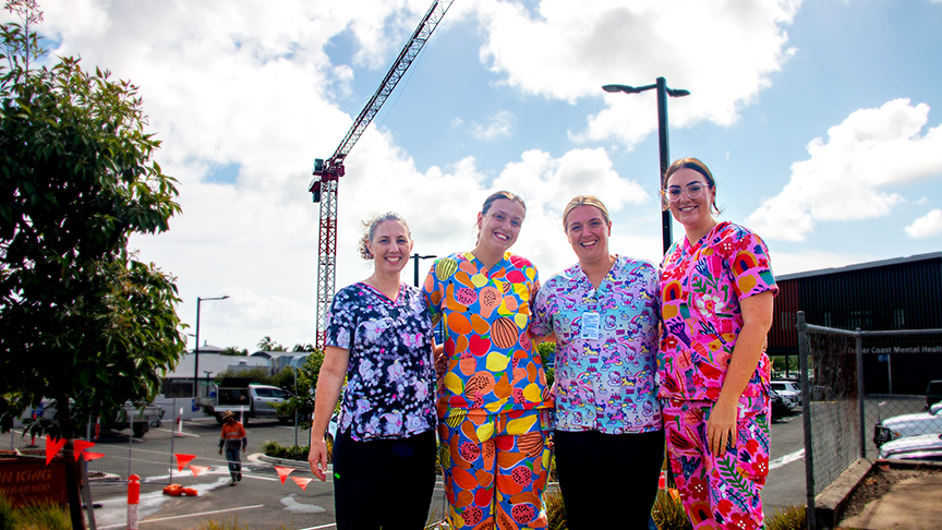 Four paediatric nurses standing in front of a tower crane that is being used for an expansion project