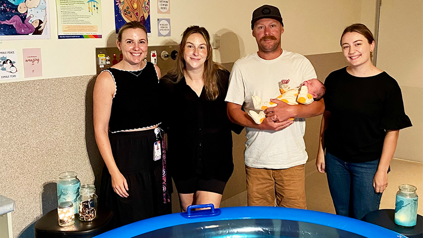 Two midwives standing with new parents in front of inflatable birthing pool