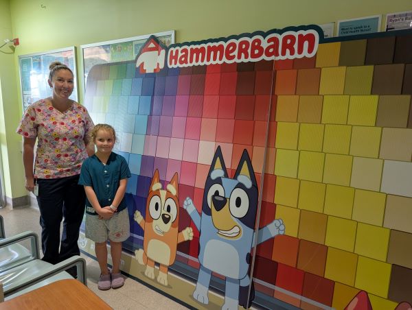 A nurse and child standing near a colourful wall with Bluey cartoon characters