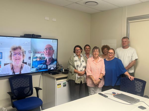 A group of people next to a TV screen showing two people connected online